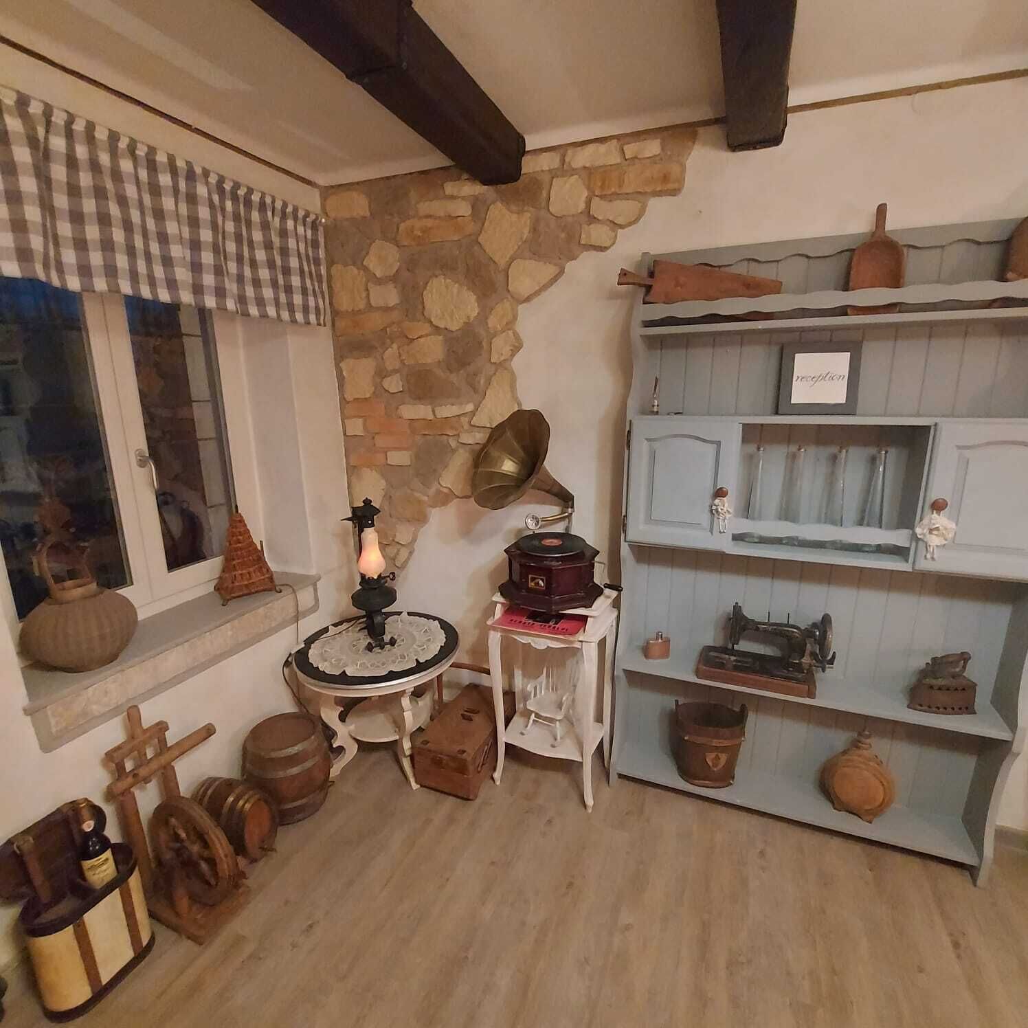 Una habitación rústica con pared de piedra, muebles de madera y objetos antiguos como un tocadiscos y una máquina de coser.