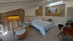 Un dormitorio con pared de piedra, una cama con toallas, una silla, una mesa y una lámpara.