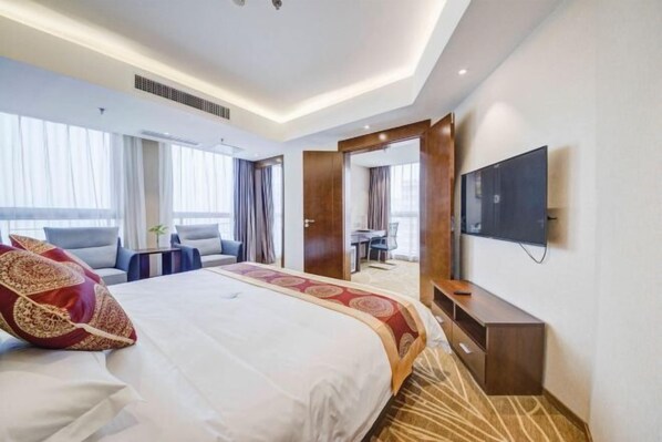 Ein Hotelzimmer mit einem großen Bett, einem Fernseher, einem Schreibtisch und Blick auf die Stadt.