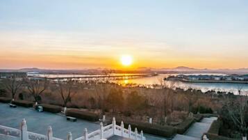 A sunset view from a terrace with a railing, overlooking a body of water and distant mountains.