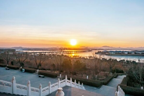 A sunset view from a terrace with a railing, overlooking a body of water and distant mountains. - Jianguo Hotel (Qian'an)