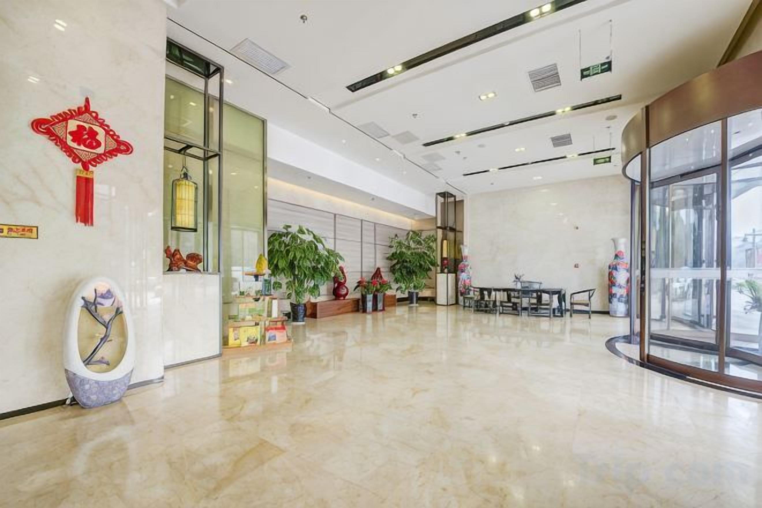 A spacious lobby with a marble floor, a reception desk, and potted plants.
