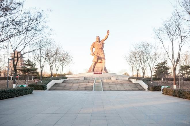 A large outdoor statue with a raised arm, surrounded by a paved area with steps leading up to it.