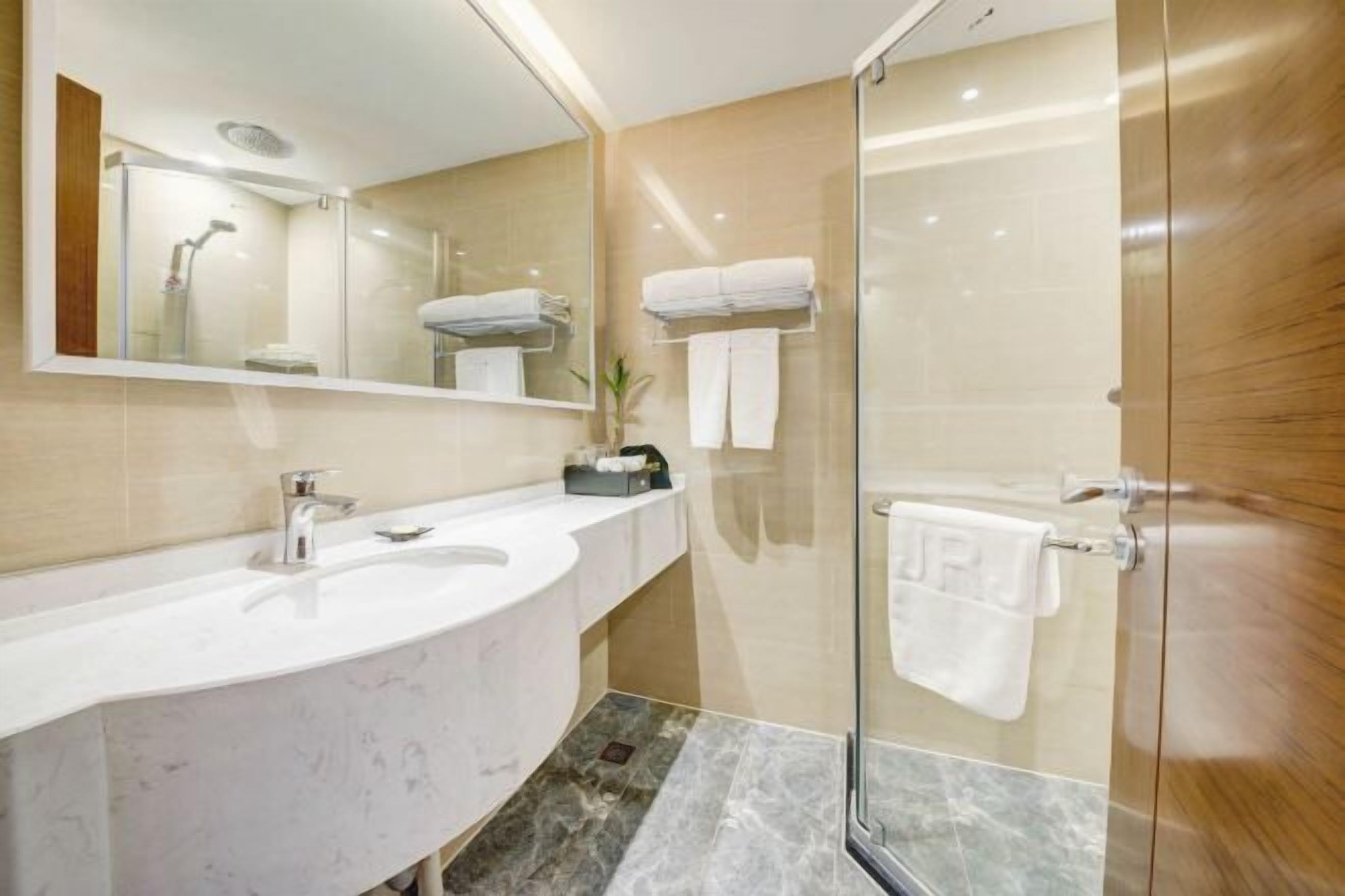 Un baño moderno con un lavabo de mármol, cabina de ducha con mampara de cristal y un espejo sobre el lavabo.