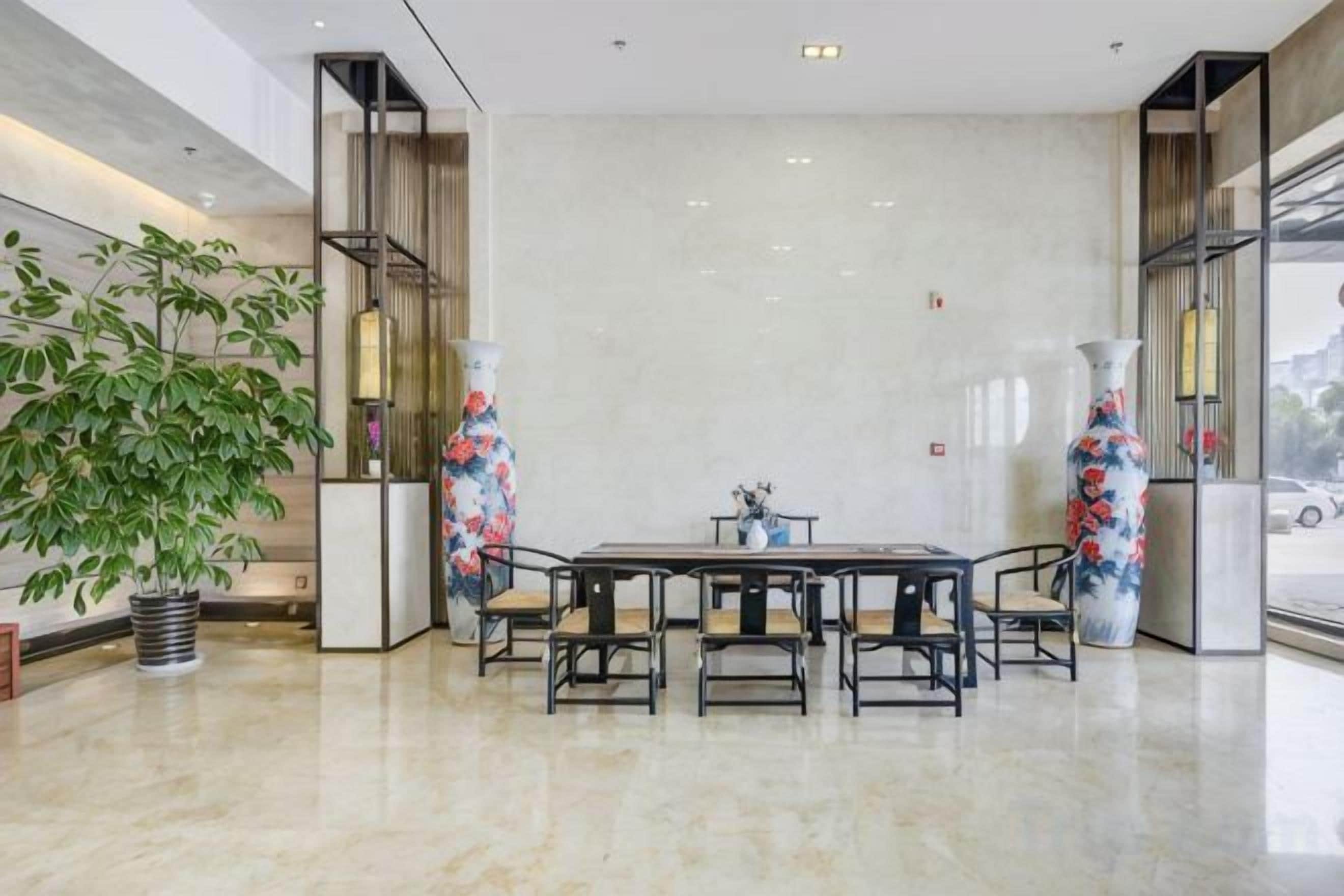 A modern hotel lobby with a marble floor, a central dining table, and two large vases with floral patterns.