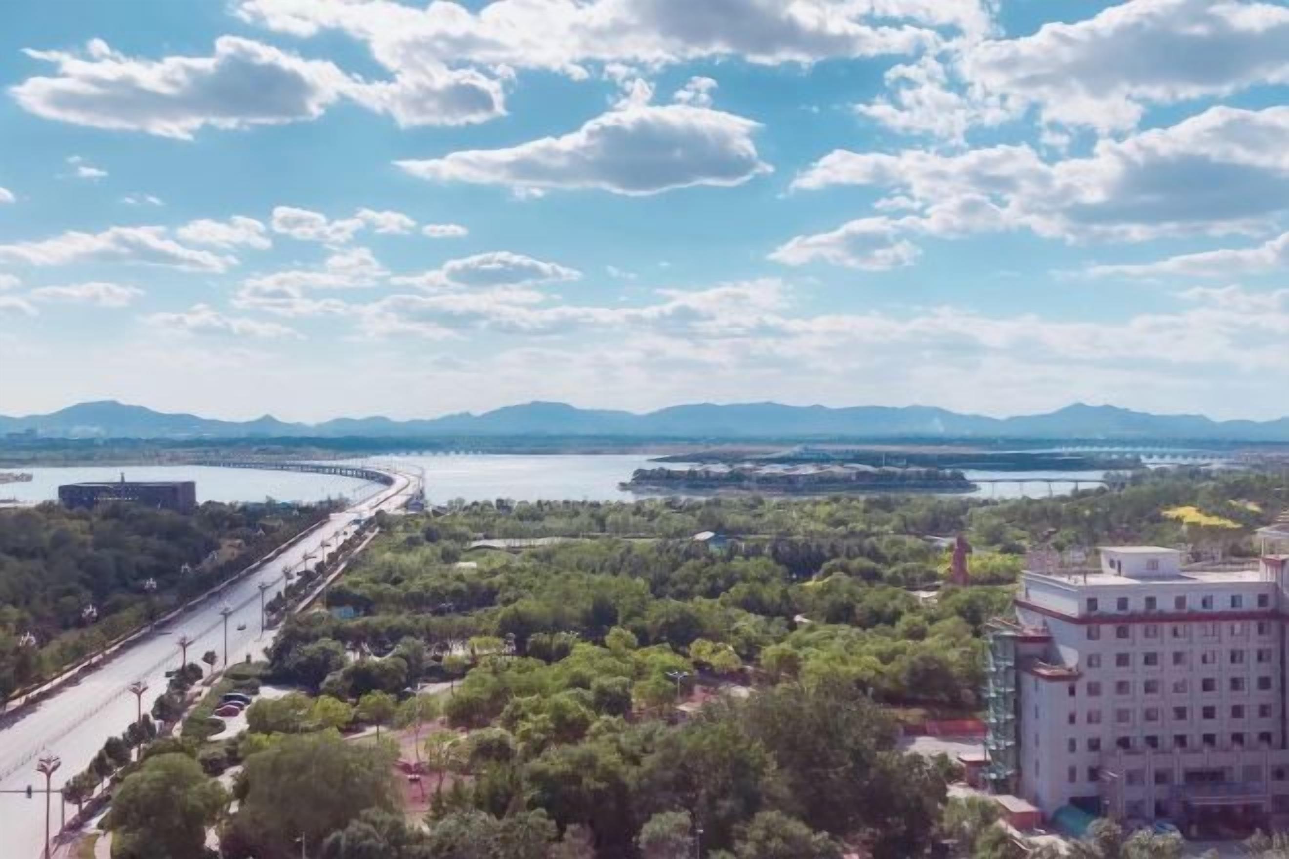 A river with a bridge, greenery, and distant mountains.