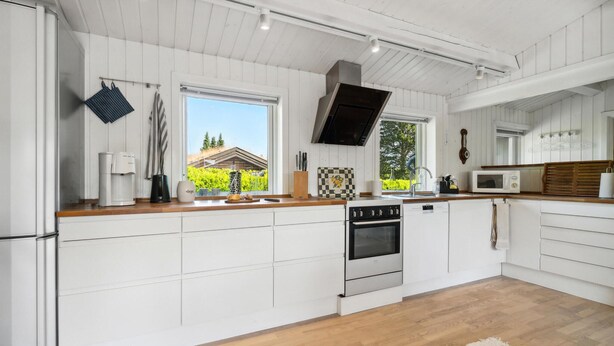 A modern kitchen with white cabinetry, a wooden countertop, a built-in oven, and a large window offering a view of greenery outside. - Awesome home in Gilleleje with WiFi (Gilleleje)