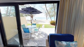 A view through a glass door to an outdoor patio with a table, chairs, and an umbrella. - Awesome Oceanfront Grd Flr Condo on Spectacular 7 Mile Beach – #19 TIC (Grand Cayman)