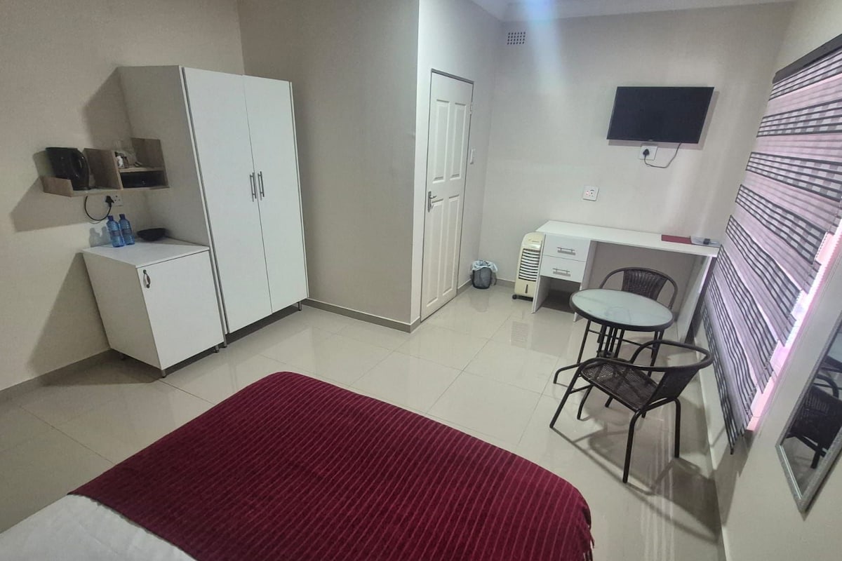 Ein kleines Hotelzimmer mit Bett, Schreibtisch, Stuhl, Fernseher und Kleiderschrank.