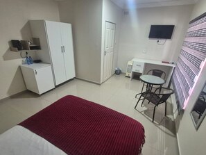 Ein kleines Hotelzimmer mit Bett, Schreibtisch, Stuhl, Fernseher und Kleiderschrank.