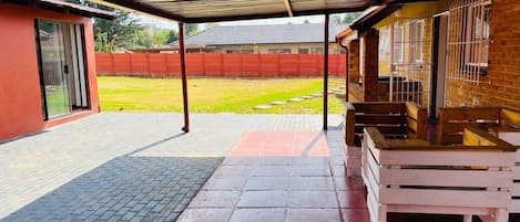 A covered patio area with a brick floor, a red wall, and a metal roof.