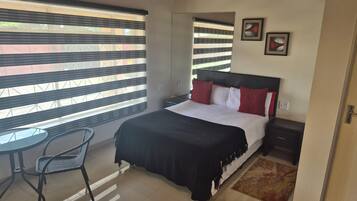 A bedroom with a bed, a nightstand, a chair, and a window with blinds.
