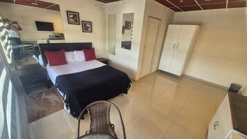 A hotel room with a bed, a desk, a chair, a wardrobe, and a TV.