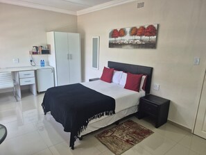 Een slaapkamer met een bed, nachtkastje en bureau met stoel. Er is een kast en een schilderij aan de muur.