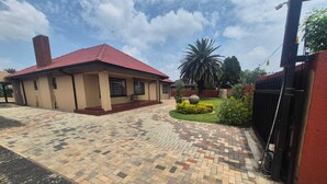 A building with a red roof, a paved entrance area, and a garden with a palm tree.