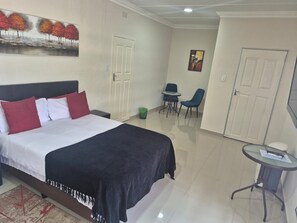 Une chambre d’hôtel avec un lit, une petite table et des chaises, un tableau au mur et une porte.