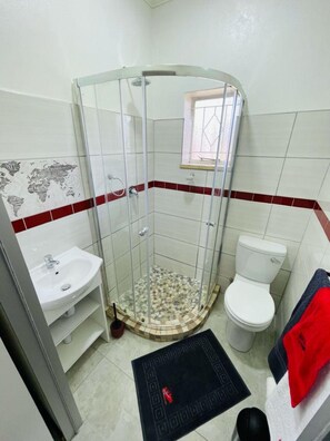 Een badkamer met een douchecabine van glas, een witte wastafel en een toilet.