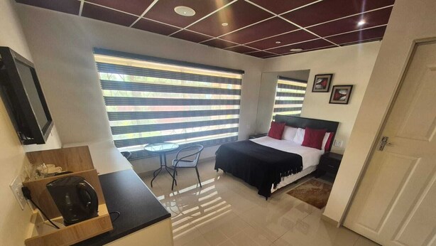 A modern hotel room with a bed, a small desk, a chair, and a window with blinds.