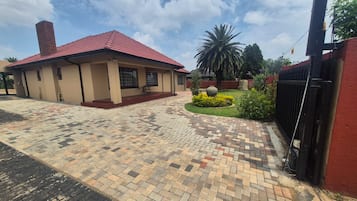A building with a red roof, a paved entrance area, and a garden with a palm tree.