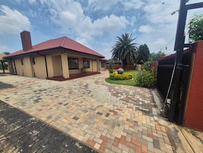A building with a red roof, a paved entrance area, and a garden with a palm tree.