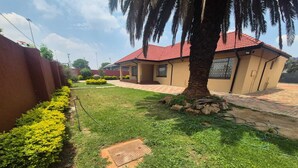 A residential area with a house featuring a red-tiled roof, a palm tree, and a well-maintained lawn.