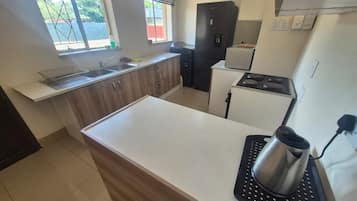 A kitchen with a white countertop, a sink, a black refrigerator, and a stove.