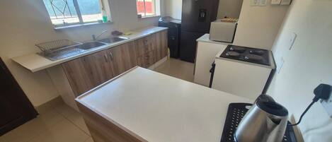 A kitchen with a white countertop, a sink, a black refrigerator, and a stove.