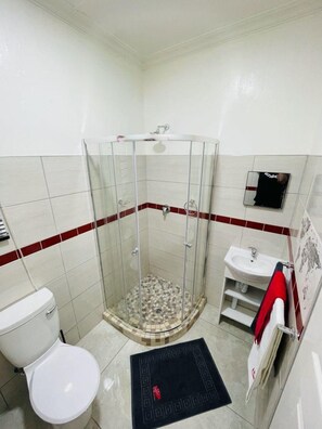 Une salle de bain avec une douche à parois de verre, des toilettes, un lavabo et un mur recouvert de carreaux rouges.