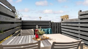 A wooden deck with a table and chairs, a potted plant, and a bottle of red drink. - Amazing apartment in Ebeltoft with WiFi (Ebeltoft)