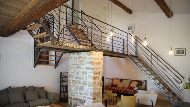 A spacious living area with a stone pillar, a staircase with a metal railing, and a sofa. - La Bastide des Oliviers (COTIGNAC)