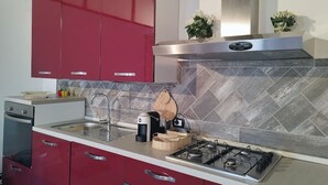 A modern kitchen with red cabinets, a stainless steel range hood, a gas stove, and a tiled backsplash. - A True Sicilian guesthouse with Pool on Mt. Etna, perfect for Families & Groups. (Puntalazzo)