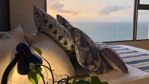 Ein Schlafzimmer mit großem Fenster, einem Bett mit gestreiften Kissen, einer Pflanze und einem Kopfhörerpaar auf dem Bett.