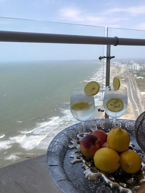 A balcony with a view of the sea and a table with fruits and glasses of water.