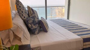 Ein Hotelzimmer mit einem Bett, Kissen, einem Streifenmuster-Teppich und Blick aufs Meer.