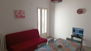 Un dormitorio con un sofá rojo, una cama con colcha estampada, un televisor sobre un mueble bajo y una lámpara colgante roja.