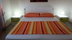Una cama bien hecha con ropa de cama a rayas, dos mesitas de noche con lámparas, una obra de arte en la pared y un mueble auxiliar verde.