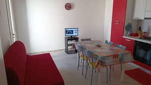 Una cocina moderna con armarios rojos, una mesa de comedor con sillas, un televisor sobre un mueble bajo y un sofá rojo.