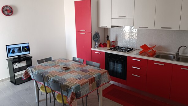 Una cocina moderna con muebles de cocina rojos y blancos, una mesa de comedor con mantel colorido y una lámpara colgante roja.