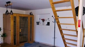 Un salon avec une armoire en bois, un canapé gris, une échelle en bois et un lampadaire.