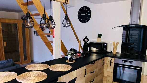 Une cuisine moderne avec un plan de travail noir, des armoires en bois, une cuisinière noire et une horloge noire accrochée au mur.