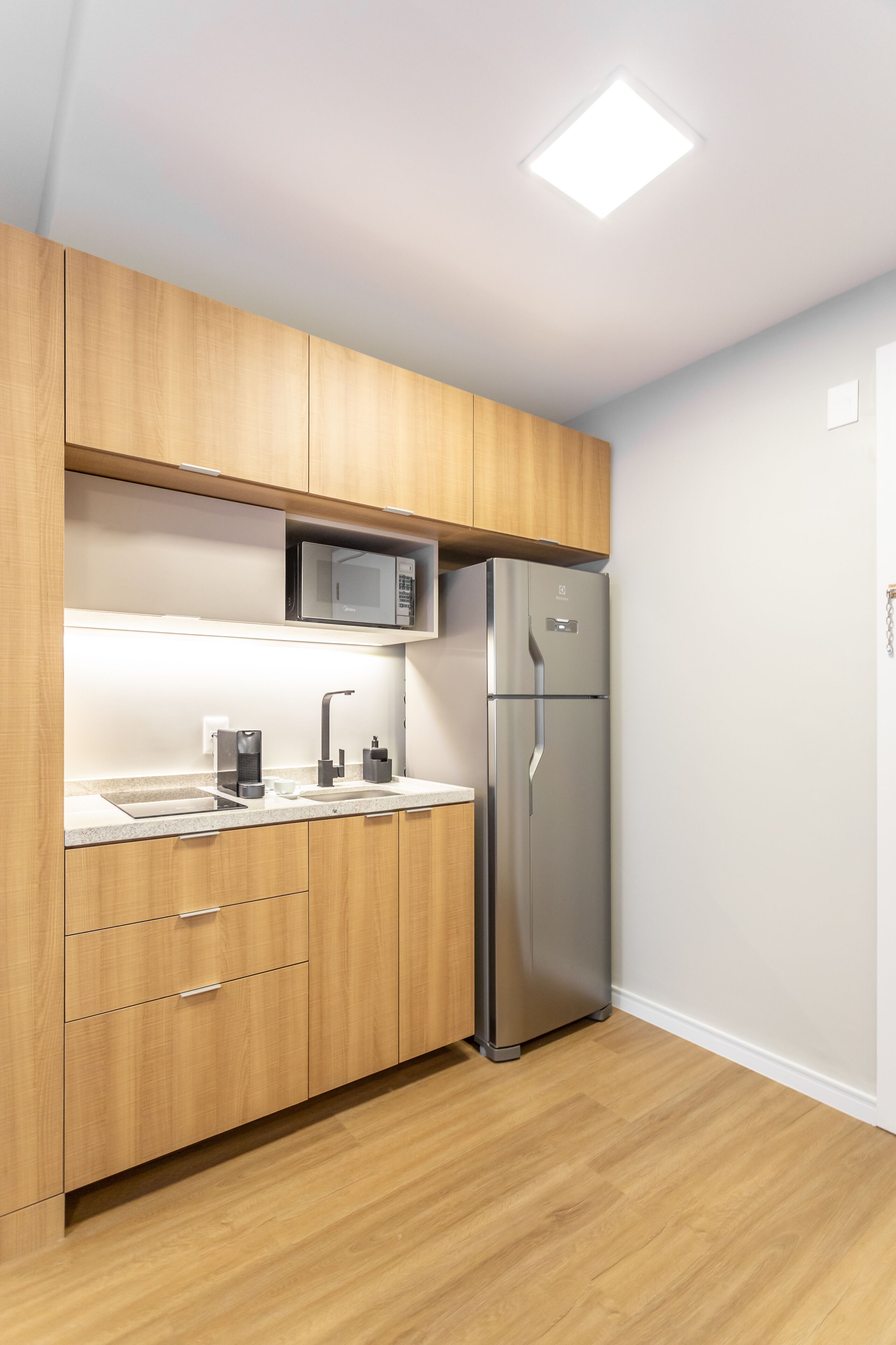 A modern kitchen with wooden cabinets, a stainless steel refrigerator, a microwave, and a coffee maker.
