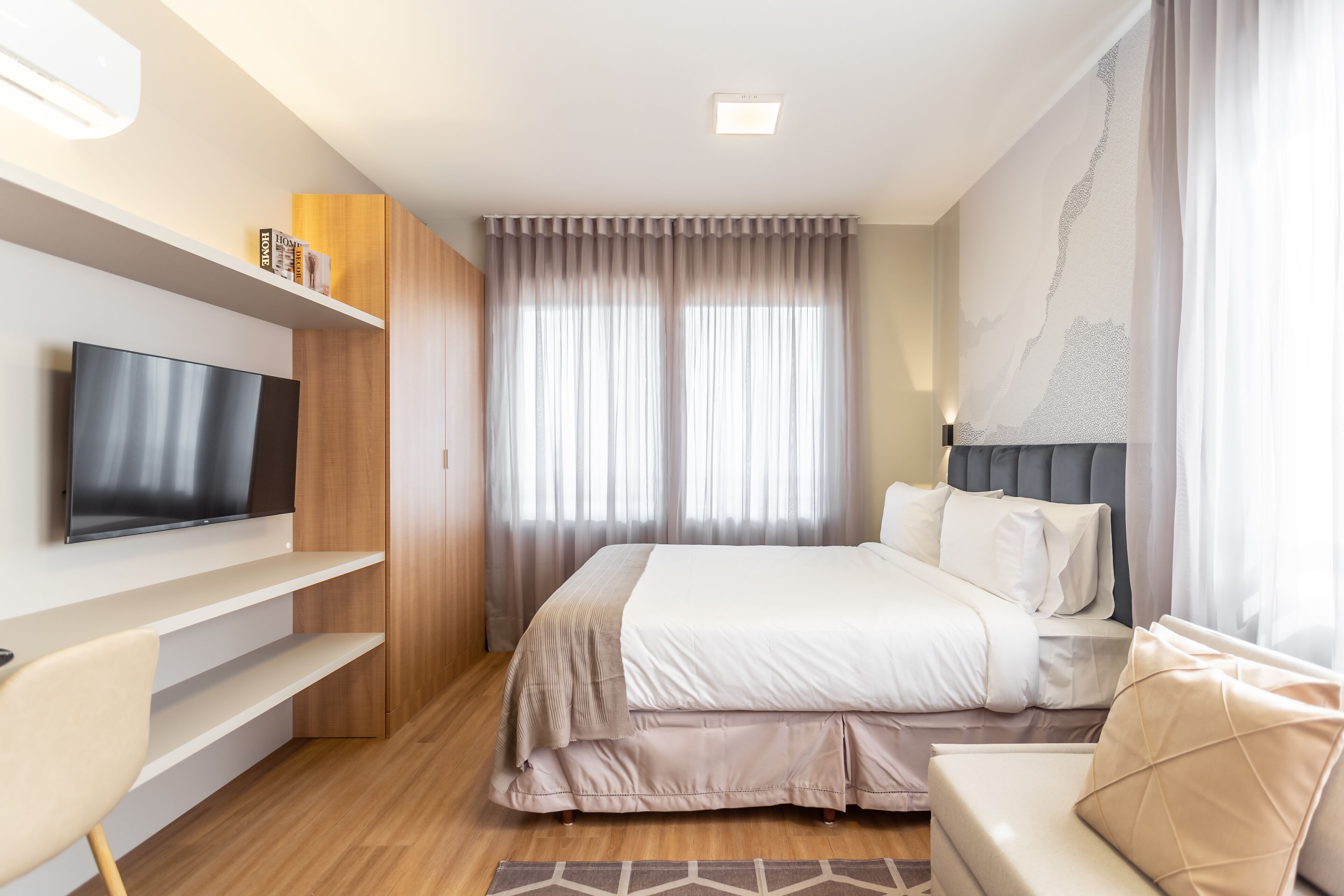 A modern hotel room with a flat-screen TV, a bed with a headboard, a sofa, and a wooden floor.