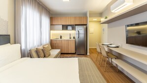 Una habitación de hotel moderna con cama, sofá, zona de comedor y kitchenette.