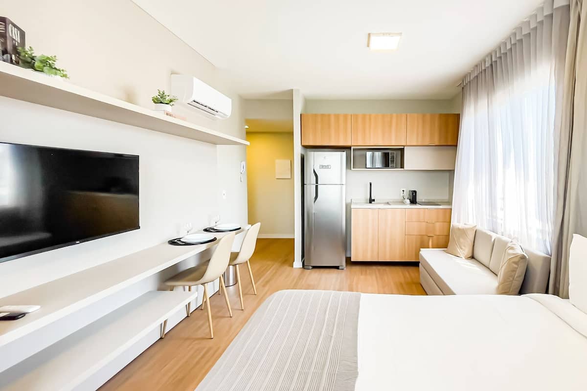 A modern hotel room with a flat-screen TV, a dining area, a kitchenette, and a sofa.