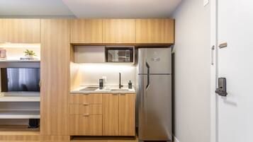 A compact kitchen with wooden cabinets, a built-in microwave, a stainless steel refrigerator, and a sink with modern faucets.