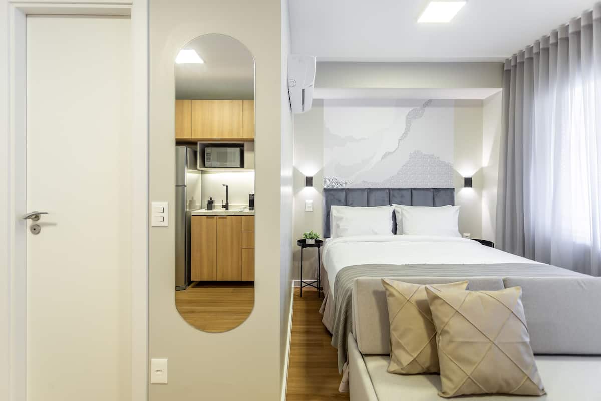 A modern hotel room with a bed, bedside table, and a view of the kitchen.