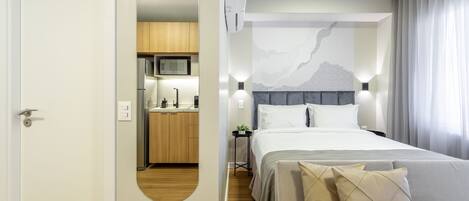 Una habitación de hotel moderna con cama, mesita de noche y vista a la cocina.