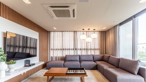 Una sala de estar moderna con un sofá seccional, un televisor de pantalla plana, una mesa de centro de madera y un ventanal con cortinas.