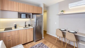 Una cocina moderna con armarios de madera, un refrigerador de acero inoxidable, un microondas integrado y un comedor con dos sillas y una mesa.