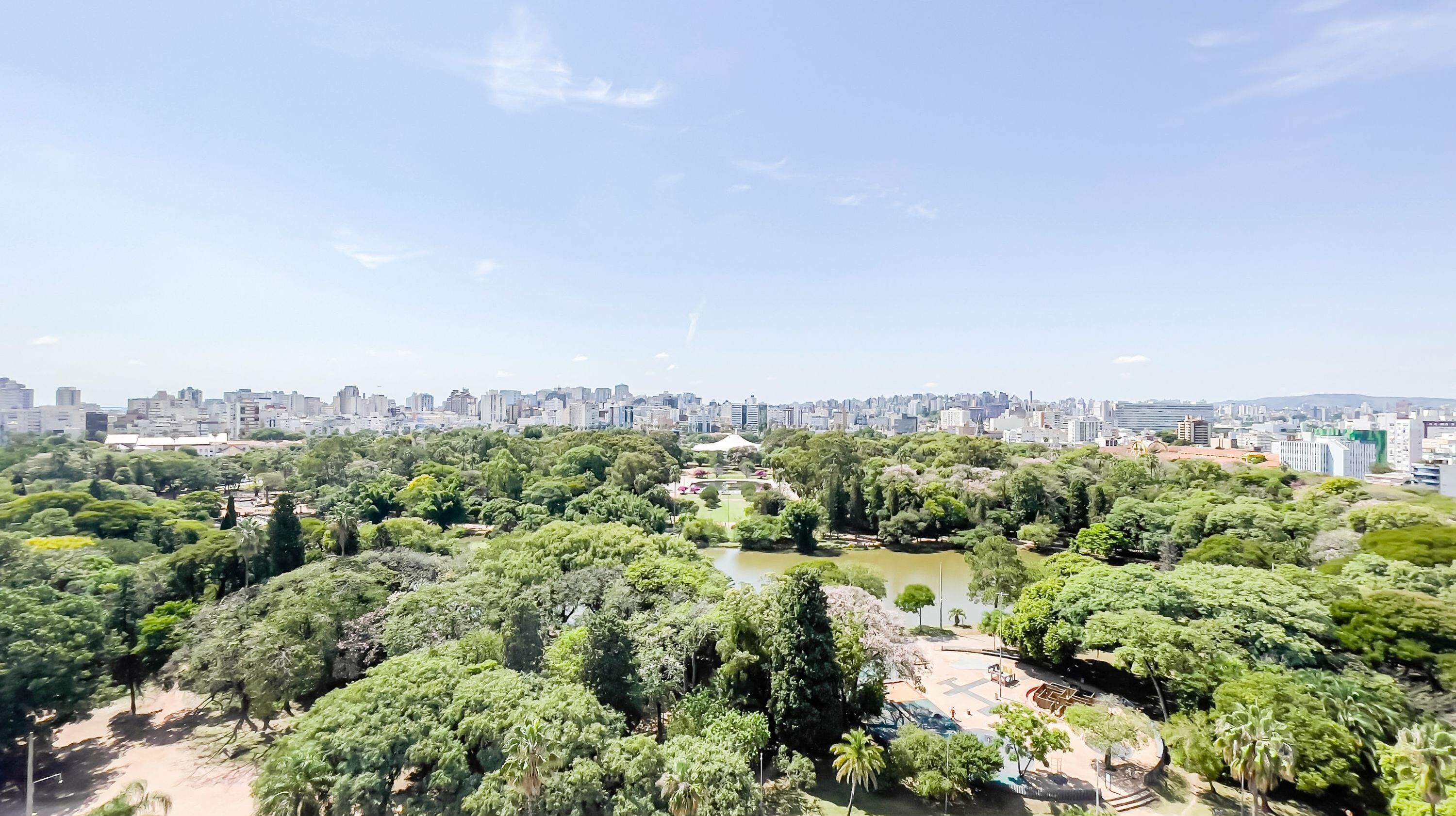A cityscape with a park featuring a pond and various trees.